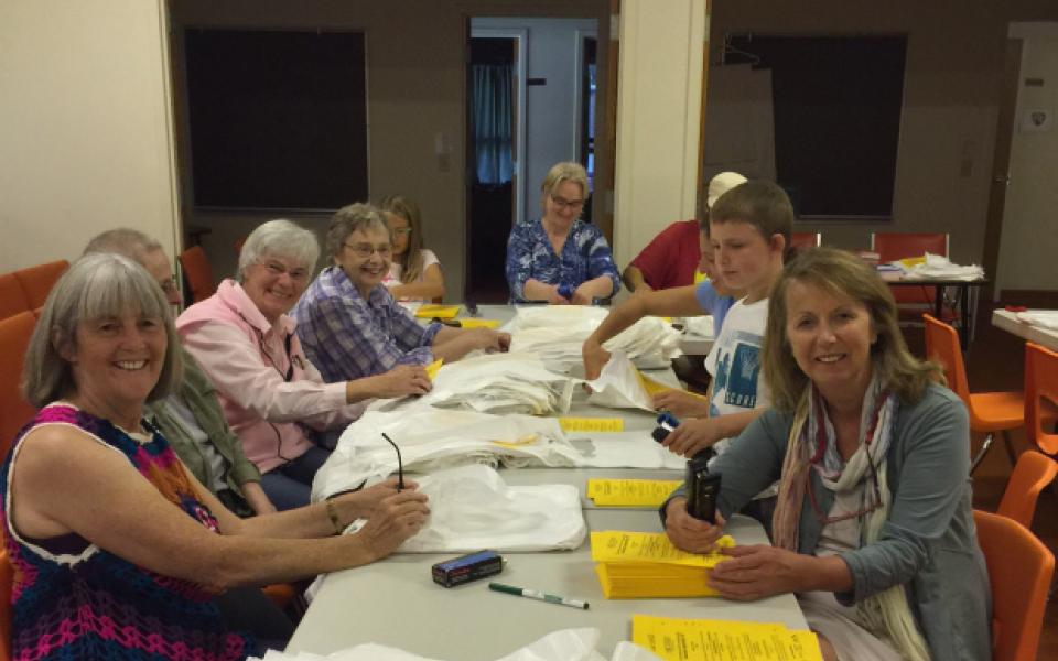 People sit at a long table smiling and stapling flyers.